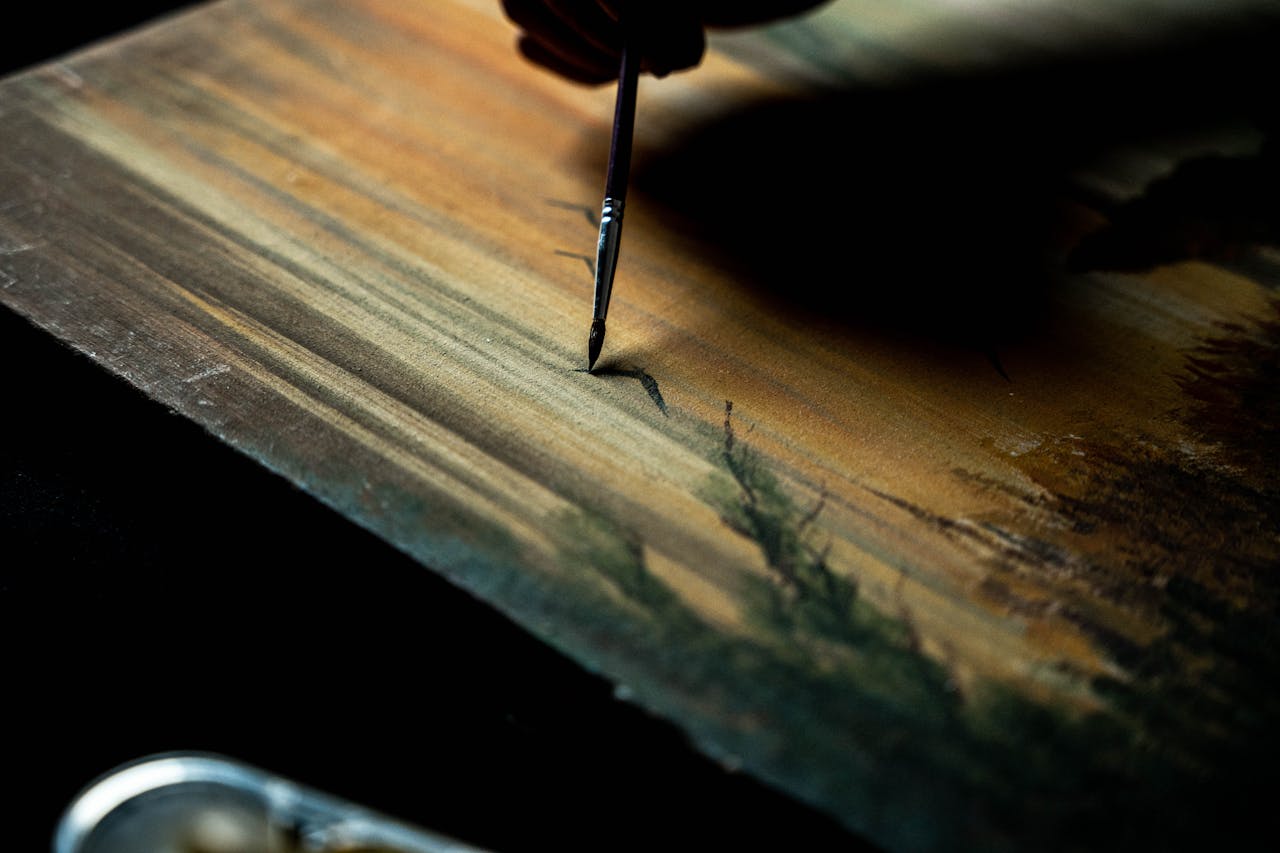 Close-up of a hand painting a serene landscape on canvas with a brush.